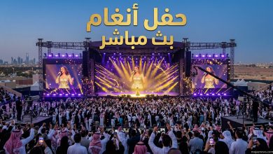 مسرح ضخم مضاء باللون الذهبي يمتلئ بالجمهور خلال حفل غنائي في السعودية، مع نص بارز يوضح القنوات الناقلة لحفل أنغام اليوم بث مباشر