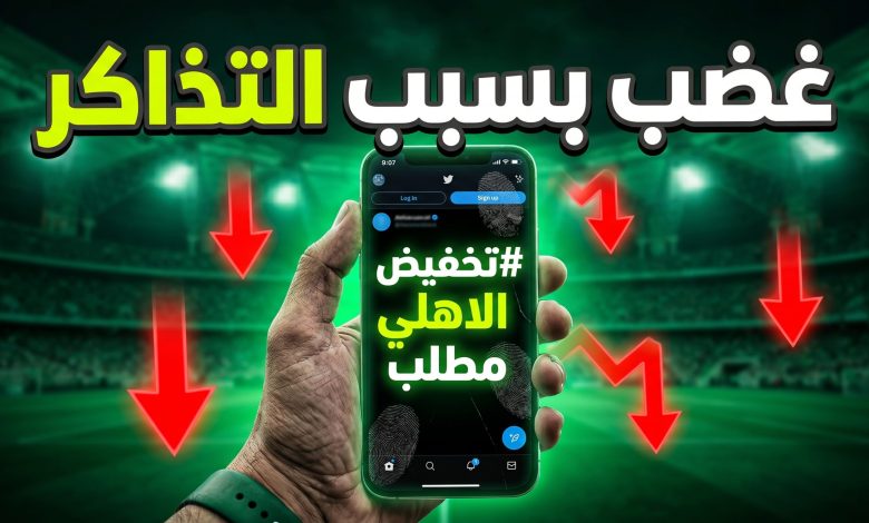هاتف ذكي يعرض هاشتاج مطالبة بتخفيض التذاكر بخلفية لملعب كرة قدم مضاء باللون الأخضر.